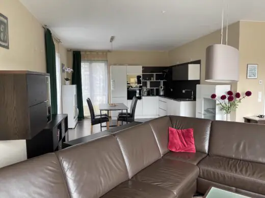 Wohnzimmer mit Ledersofa, im Hintergrund Küche mit Essbereich