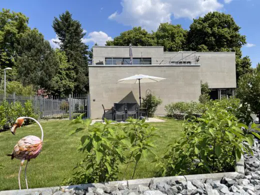 Gästegarten mit Rasen, Büschen und Flamingo-Figur, im Hintergrund das Haus