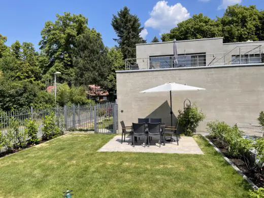 Gästegarten mit Rasen und Sitzgruppe unter einem Sonnenschirm, dahinter das Haus