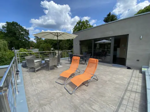 Dachterrasse mit orangefarbenen Liegen, Sonnenschirm und Geländer