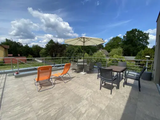 Weite Dachterrasse mit Liegen und Sitzgruppe unter Wolkenhimmel