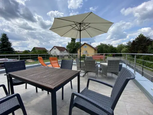 Dachterrasse mit Holztisch, Stühlen und Sonnenschirm, im Hintergrund Wohnhäuser