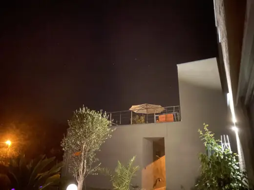 Haus bei Nacht mit Olivenbaum im Garten und beleuchteter Hauswand