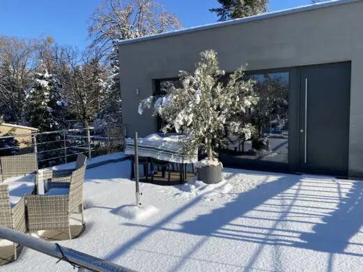 Verschneite Dachterrasse mit Gartenmöbeln und Schnee auf einem Bäumchen